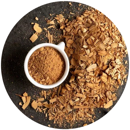 A small white bowl of reddish-brown muira puama powder among pale wood chips on a dark round plate
